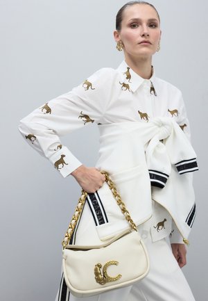 Camisa blanca con estampado de leopardo dorado y un collar, combinada con una chaqueta blanca con rayas negras. Accesorio: bolso blanco con cadena dorada y logotipo.