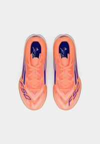 Lyse koralfarvede fodboldsko med lilla detaljer og striber, der har en struktureret overdel og et strømlinet design til præstation.