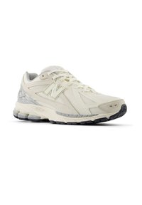 Beige and gray athletic sneaker with mesh and suede textures, black sole, and "N" logo on the side.