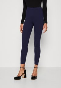 Leggings extensibles bleu marine avec une taille haute, un design ajusté et une texture lisse, accompagnés de chaussures à talons carrés noires.