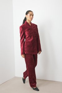 Blazer de terciopelo carmesí con solapa y bolsillos, combinado con pantalones a juego, complementado con unos zapatos de tacón negros y afilados.
