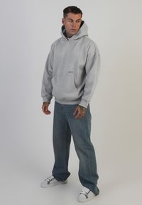 Grauer Kapuzenpullover mit Fronttasche und Logo, kombiniert mit hellblauen, lässigen Jeans und weißen Sneakers mit grauen Akzenten.