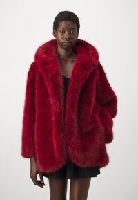 Rød faux fur jakke med stor hette, løs passform, sidelommer og en myk, fluffy tekstur, kombinert med en svart topp og kort skjørt.