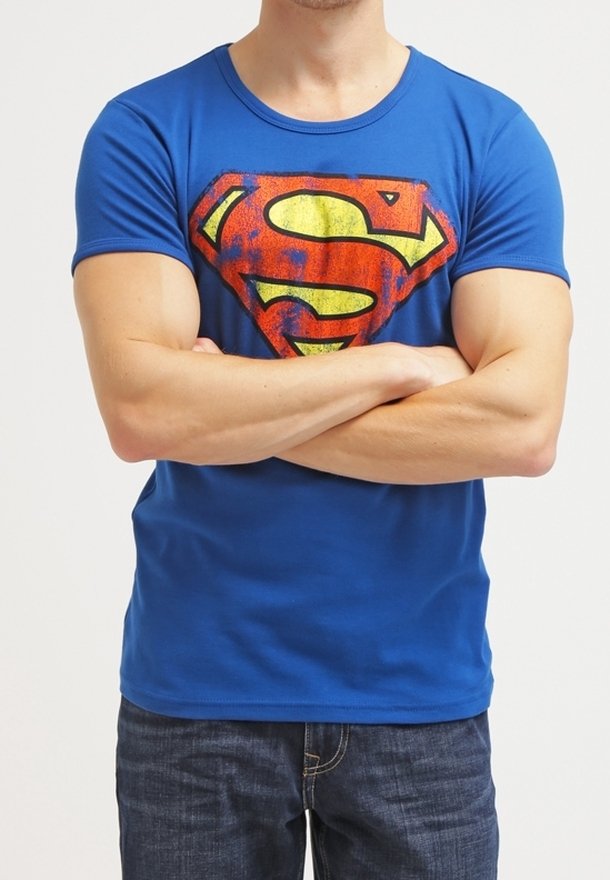 Niebieska bawełniana koszulka z dużym czerwono-żółtym logo Supermana na piersi. Krótkie rękawy i okrągły dekolt. Nosi się ją z ciemnymi dżinsami.
