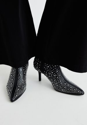 Stivaletti neri alla caviglia con punta affusolata, caratterizzati da decorazioni in perline d'argento e un tacco a stiletto alto. Chiusura con zip sul retro.