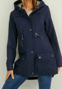 Voděodolná parka tmavě modré barvy s kapucí, stahováním v pase, zapínáním na zip a patentní knoflíky a předními kapsami se klopami.