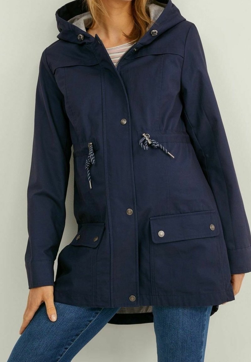 Voděodolná parka tmavě modré barvy s kapucí, stahováním v pase, zapínáním na zip a patentní knoflíky a předními kapsami se klopami.