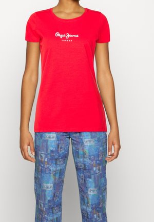 Persoon draagt een rood Pepe Jeans London t-shirt en een blauwe broek met een digitaal patroon met ogen en abstracte vormen.