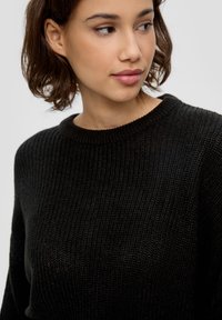 Schwarzer gestrickter Pullover mit Rundhalsausschnitt, der ein strukturiertes Muster aufweist. Der Stoff wirkt weich und bequem.