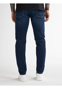 Tmavě modré džíny s úzkým střihem, pěti kapsami, lehkým vyblednutím a pohodlným pasem, doplněné bílými teniskami.