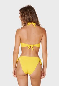 Žlutý bikinový set se zavazovacím halter topem a nízkými kalhotkami se šněrováním po stranách, vyrobený z hladké, elastické tkaniny.