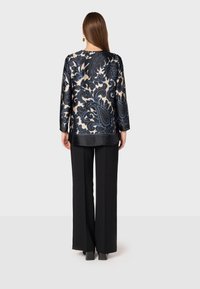 Blusa a maniche lunghe in satin nero con motivo paisley blu, abbinata a pantaloni larghi neri, vista da dietro.