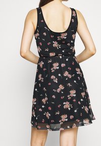 Robe noire sans manches avec un motif floral dans des tons de rose et de crème. Elle présente une taille cintrée et une jupe évasée, confectionnée dans un tissu léger.
