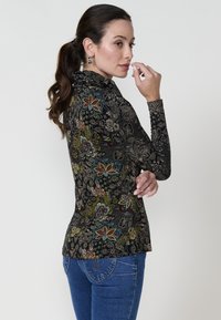 Langärmliges Top aus schwarzem Stoff mit bunten Blumenmustern. Verfügt über eine figurbetonte Silhouette und einen hohen Kragen. Jeans mit runden Gesäßtaschen.