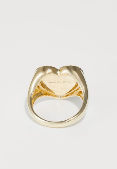 Goldring mit einer glatten, polierten Oberfläche, der an der Vorderseite ein herzförmiges Design aufweist und eingravierte Details im Inneren hat.
