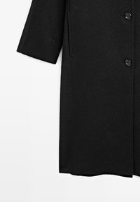 Cappotto di lana nera con silhouette dritta, maniche corte e due bottoni. La texture è morbida con una finitura liscia.