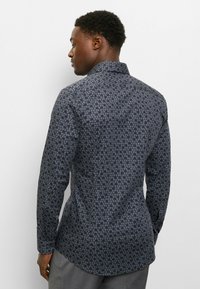 Langärmeliges Hemd aus dunklem Stoff mit dezentem Blumenmuster. Strukturierter Kragen und Manschetten, schlanke Passform und abgerundeter Saum.