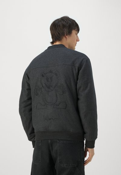Chaqueta bomber gris oscuro con puños acanalados, que presenta un diseño de oso bordado en la parte posterior y un detalle característico cerca del dobladillo.
