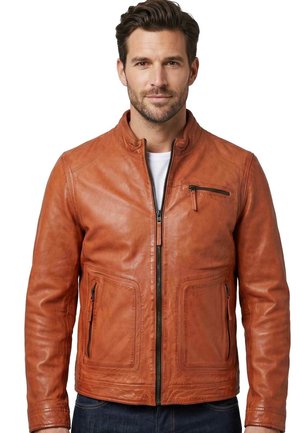 Man wearing a tan leather jacket with front zipper, zippered chest pocket, and two zippered side pockets, over a white shirt and blue jeans.