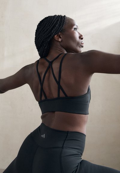 Sort atletisk sports-bh med detaljeret stropdesign og højtaljede sorte leggings. Glat tekstur, tætsiddende stil og minimalistisk branding.