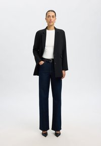 Musta bleiseri valkoisen paidan päällä, yhdistettynä korkeavyötäröisiin tummiin farkkuihin ja mustiin kärkitossuihin. Siistit linjat ja strukturoitu istuvuus.