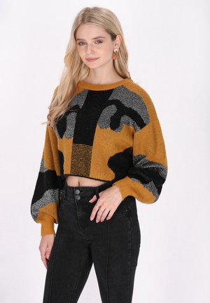 Krótki sweter dziany w musztardowym kolorze z czarnymi i srebrnymi abstrakcyjnymi wzorami, z szerokim dekoltem i objętościowymi rękawami.