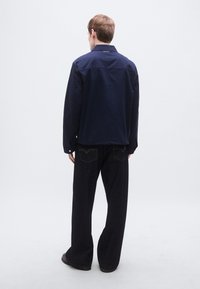 Σκούρο μπλε καθημερινό σακάκι με γιακά και μακριά μανίκια, συνδυασμένο με μαύρα παντελόνια φαρδιάς γραμμής που έχουν κίτρινη ραφή στις πίσω τσέπες.