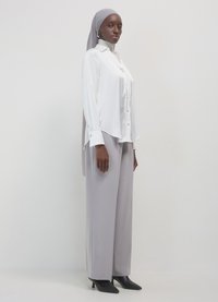 Camicia bianca a maniche lunghe con dettagli ai bottoni, abbinata a pantaloni grigi chiari a vita alta. Tacchi a punta neri completano l'outfit.