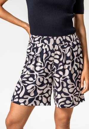 Frau trägt schwarz-weiß gemusterte Shorts mit elastischem Bund und schwarzes, geripptes Kurzarmshirt.