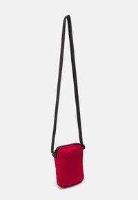 Borsa a tracolla in tessuto rosso con forma rettangolare, tracolla nera e chiusura con zip, dotata di una texture liscia e un design semplice.