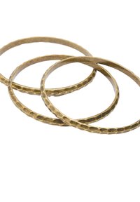 Trzy złote, mosiężne bangles. Każdy bangle jest cienki i okrągły, z teksturowaną powierzchnią i rustykalnym wykończeniem.