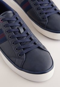 Marineblå lædersneakers med en tekstureret finish, med vævede snørebånd og en hvid gummisål. Stribede accenter i vinrød. Rundet tåsne design.