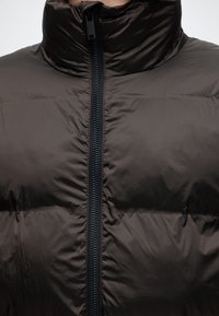 Gros plan d'une veste noire matelassée avec un col haut et une fermeture éclair visible au centre.