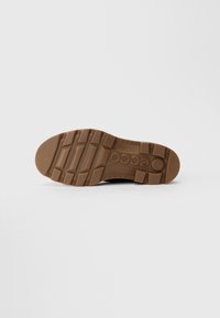 Semelle de chaussure noire avec caoutchouc marron, présentant un motif antidérapant texturé et un logo circulaire. Conception flexible adaptée à divers terrains.