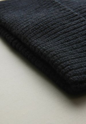 Tissu en laine noir tricoté, texturé avec des côtes verticales ; plié avec une surface douce et duveteuse, placé sur un fond gris clair.