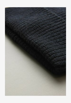 Schwarzer gestrickter Wollstoff mit vertikaler Rippstruktur; gefaltet mit einer weichen, flauschigen Oberfläche, auf einem hellgrauen Hintergrund platziert.