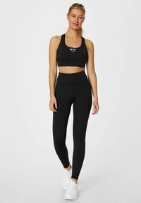 Sort sportsbh og højtaljede leggings lavet af strækbart stof, med et logo, parret med hvide træningssko.