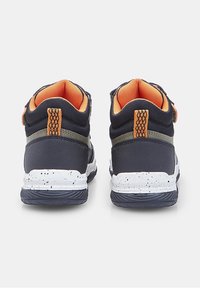 Sneakers blu navy con fodera in mesh arancione e linguette, suole intermedie macchiate di bianco e suole nere viste da dietro su uno sfondo bianco.