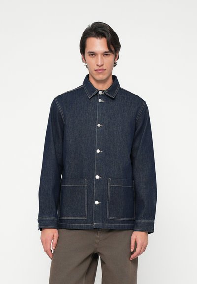 Veste en denim foncé avec un col, fermeture à boutons sur le devant, deux grandes poches, coutures blanches contrastées et une coupe ample.
