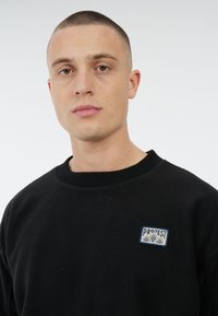 Zwarte fleece sweatshirt met een ronde halslijn en geribde boorden. Opvallend geborduurd "PROTEST" logo in een rechthoekig label op de borst.