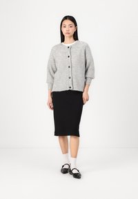 Lys grå strikket cardigan med rund hals, trekvartlange ermer og knappeåpning, sammen med et svart blyantskjørt og dekorative sko.