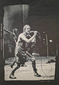 Zwarte t-shirt met een grafische print van een performer die gepassioneerd zingt, gekleed in versleten kleding, met bandleden op de achtergrond.