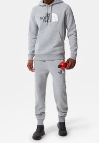 Grijze hoodie en joggers met een voorlogo, gemaakt van een katoenmix. De hoodie heeft een trekkoord en een voorzak, in combinatie met zwarte schoenen.