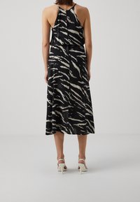 Czarna i biała prążkowana sukienka midi bez rękawów, o zwiewnym kroju i detalu z dziurką z tyłu. Noszona z białymi szpilkami.