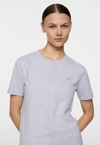 Szara koszulka z krótkim rękawem, wykonana z miękkiej bawełny, z okrągłym dekoltem i subtelne logo na lewej klatce piersiowej. Gładka faktura.