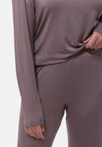 Brun långärmad topp och figurnära byxor i mjukt, texturerat tyg. Toppen hänger något, med avslappnad passform; byxorna har resårmidja.