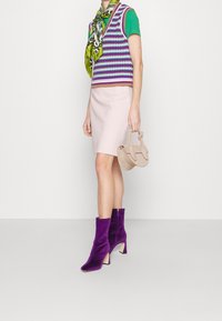 Bottes de cheville en velours violet, une jupe rose pastel, un gilet en tricot rayé violet et vert, et un sac à main beige clair.