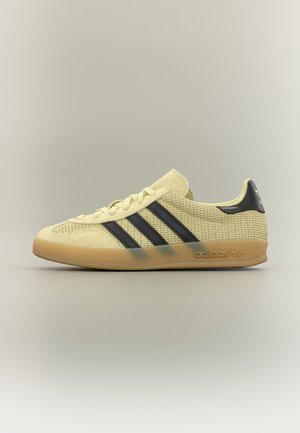 Нисък модел маратонки Adidas в бежово с черни ивици, горна част от текстурирана тъкан, гумена подметка и брандирана табелка на петата и междинната подметка.
