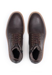 Bruine leren enkelboots met ronde neuzen, textuurvoering aan de binnenkant, metalen oogjes en bruine veters; contrasterende stiksels rond de zool.