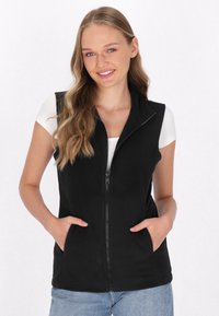 Schwarze gesteppte Weste mit hohem Kragen und zwei vorderen Taschen, aus weichem, strukturiertem Stoff. Getragen über einem weißen Oberteil und lässig gestylt.
